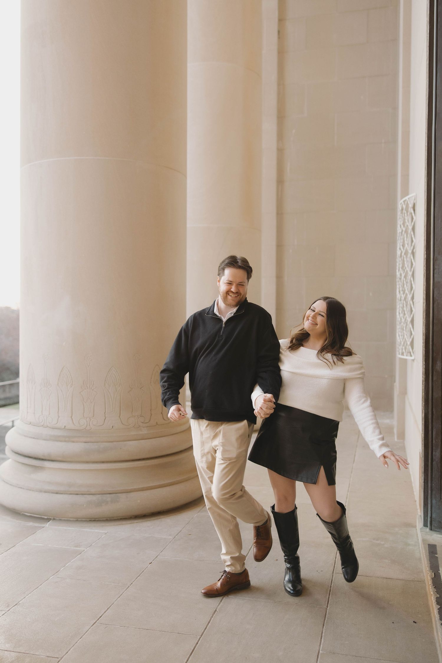 A playful couple dances and poses between white classical columns in a series of candid engagement photos.