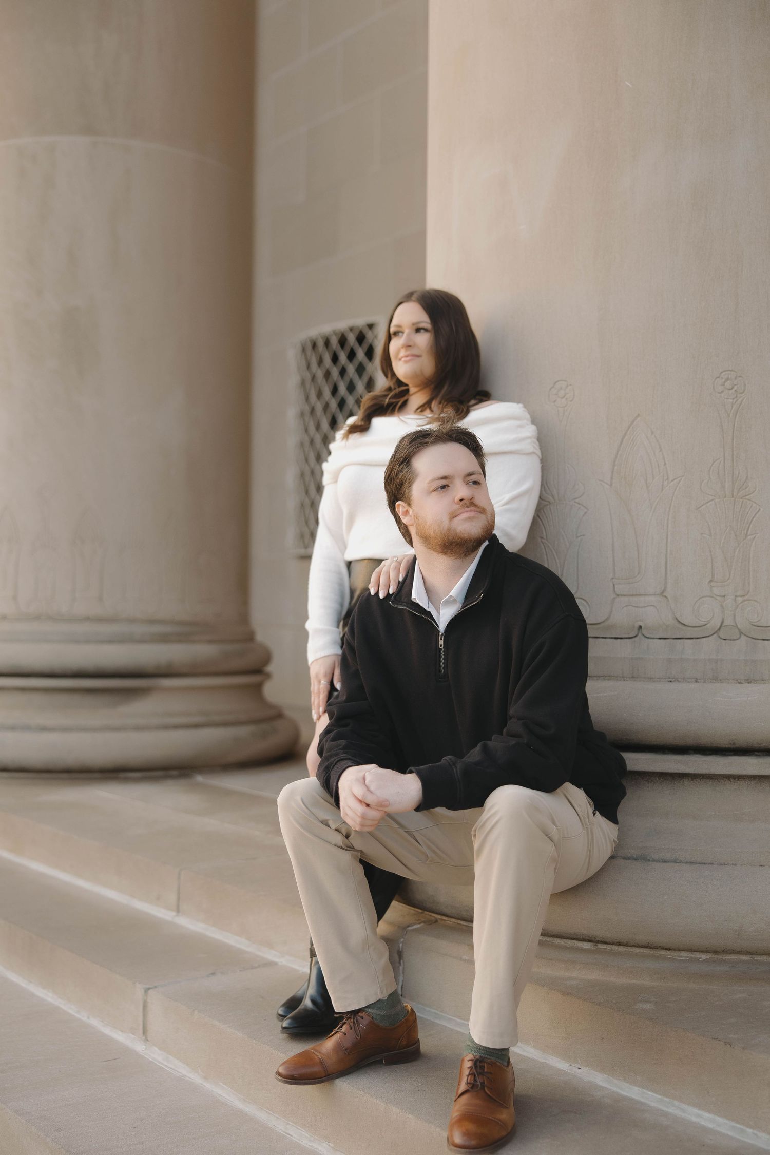 A couple poses together against white stone columns in a romantic architectural setting.