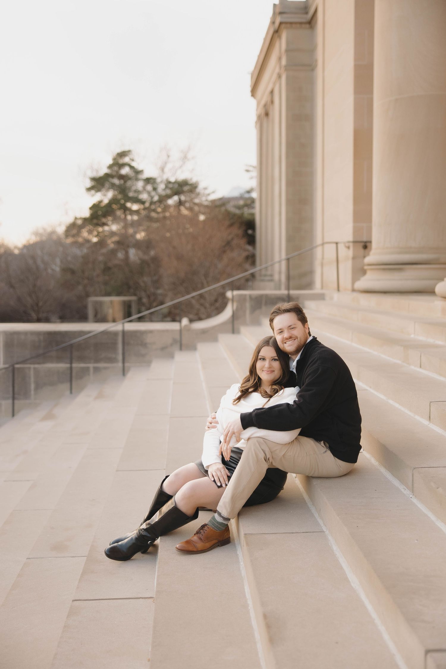 A couple sits intimately on stone steps at sunset during an engagement photoshoot.