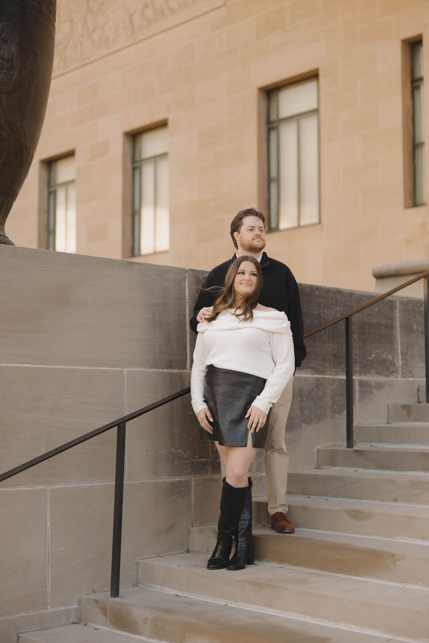 A couple poses romantically on stone steps against a beige building facade.
