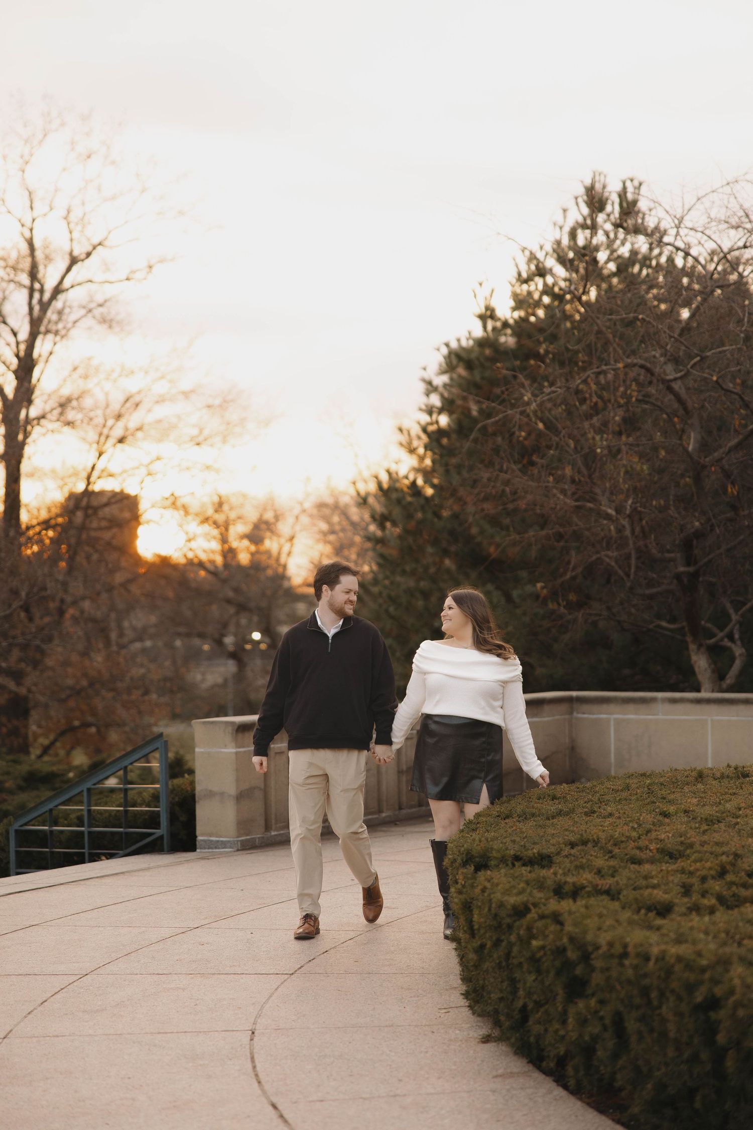 A couple walks together on a curved pathway during sunset surrounded by winter foliage.