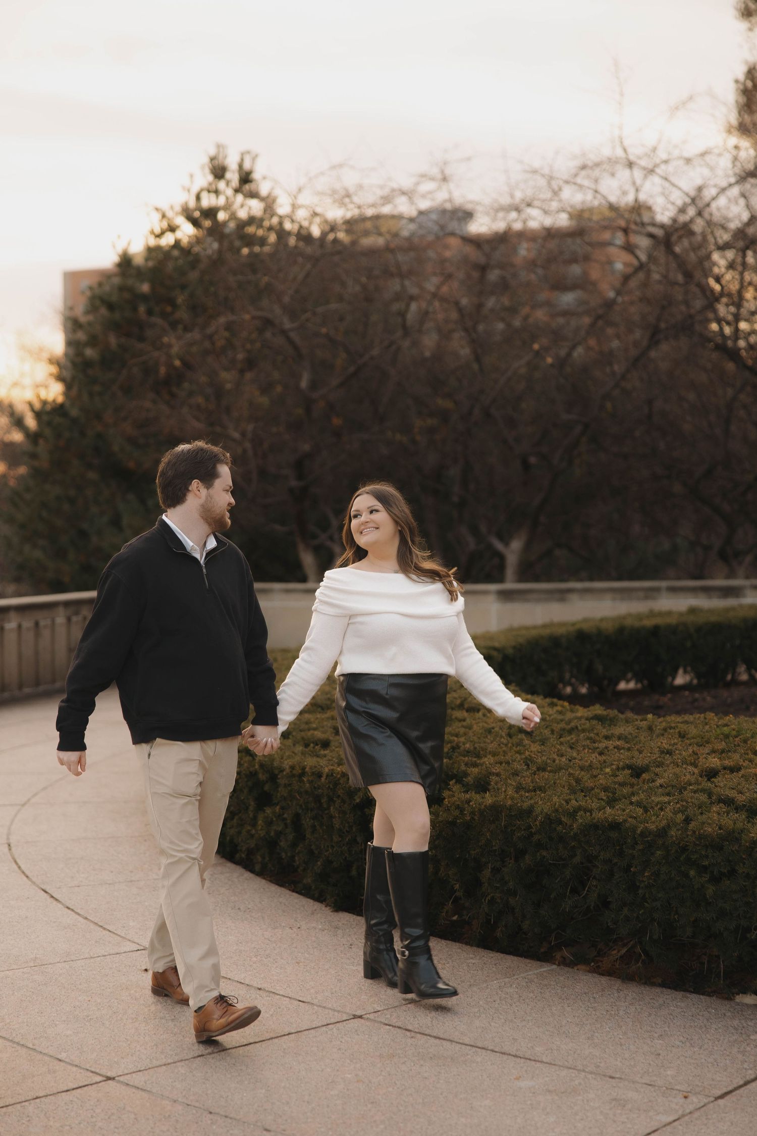 A couple walks together on a garden path at sunset, sharing a playful and romantic moment.