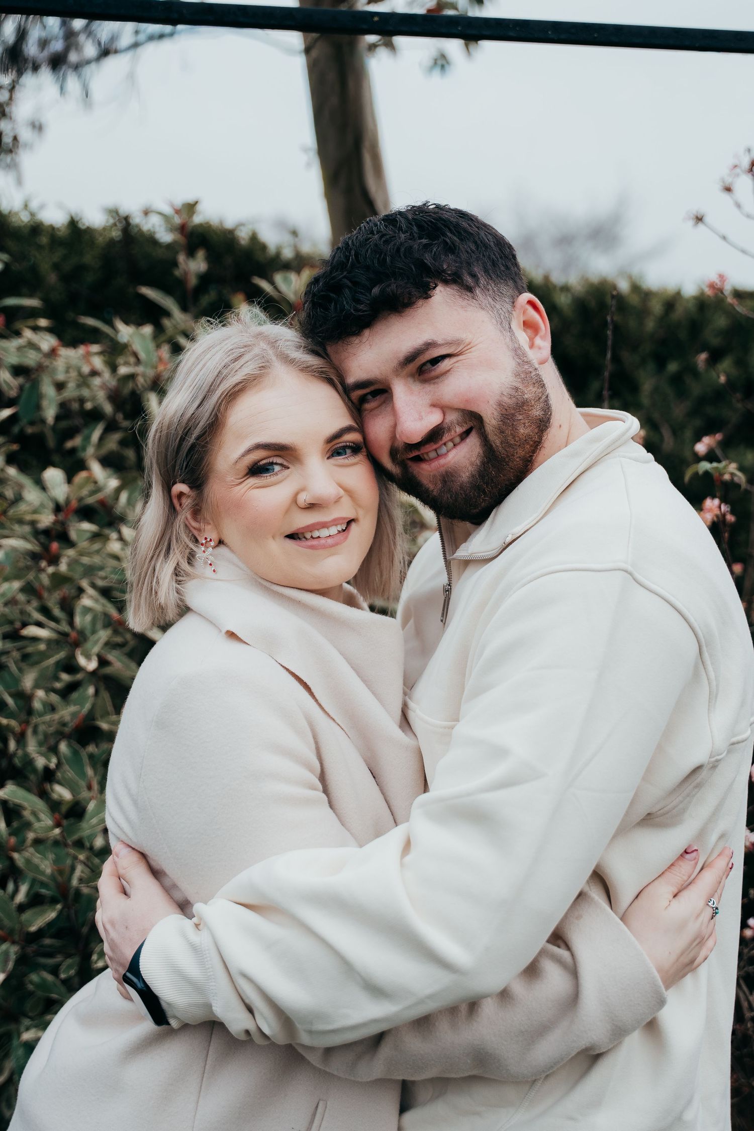 Couple embraces warmly while wearing matching cream colored outfits outdoors.