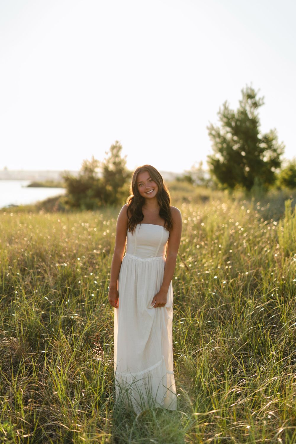 A flowing white sundress stands out against tall grass in a golden sunlit meadow during summer.