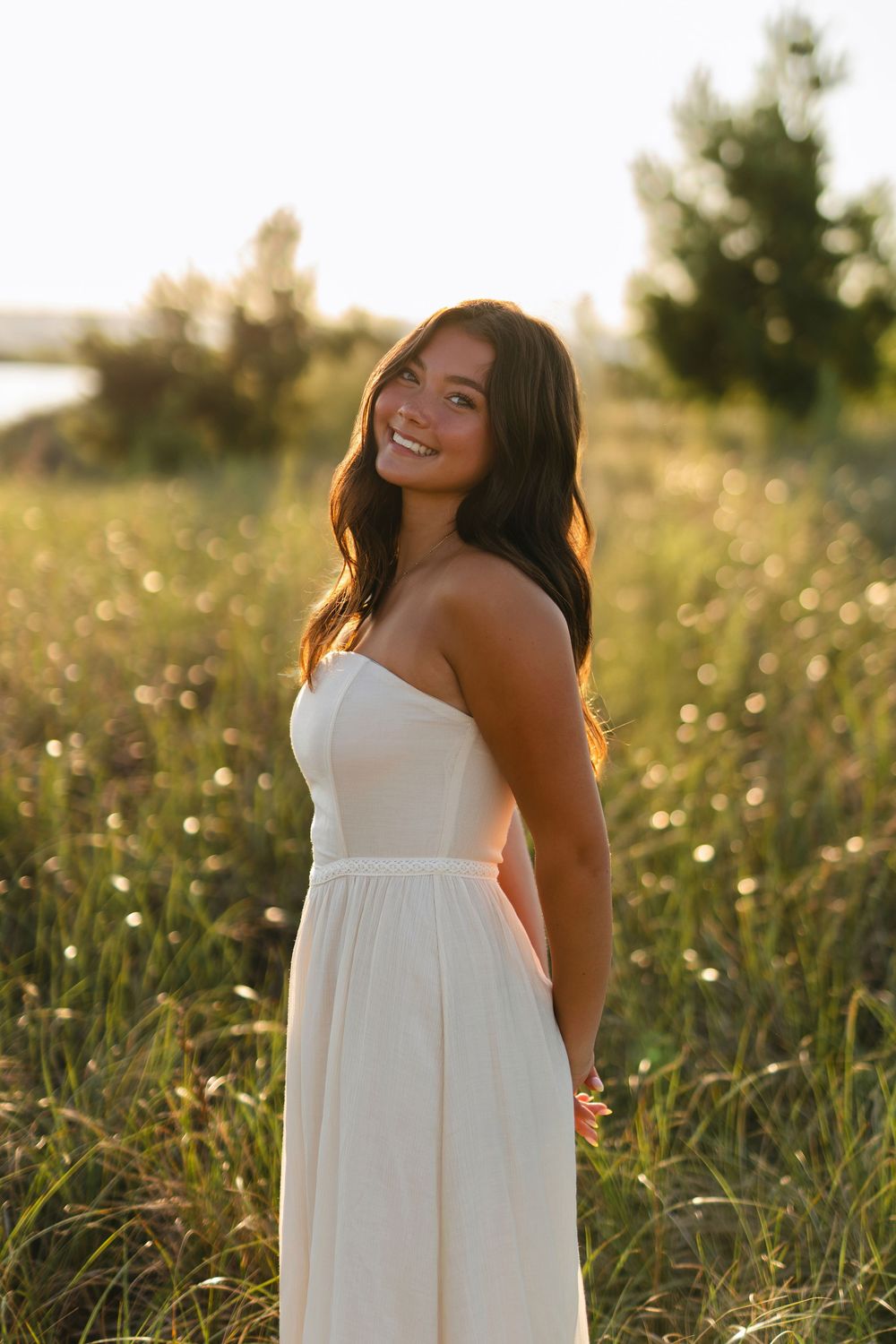 Person in white sundress poses joyfully in a summer meadow with golden sunlight filtering through.