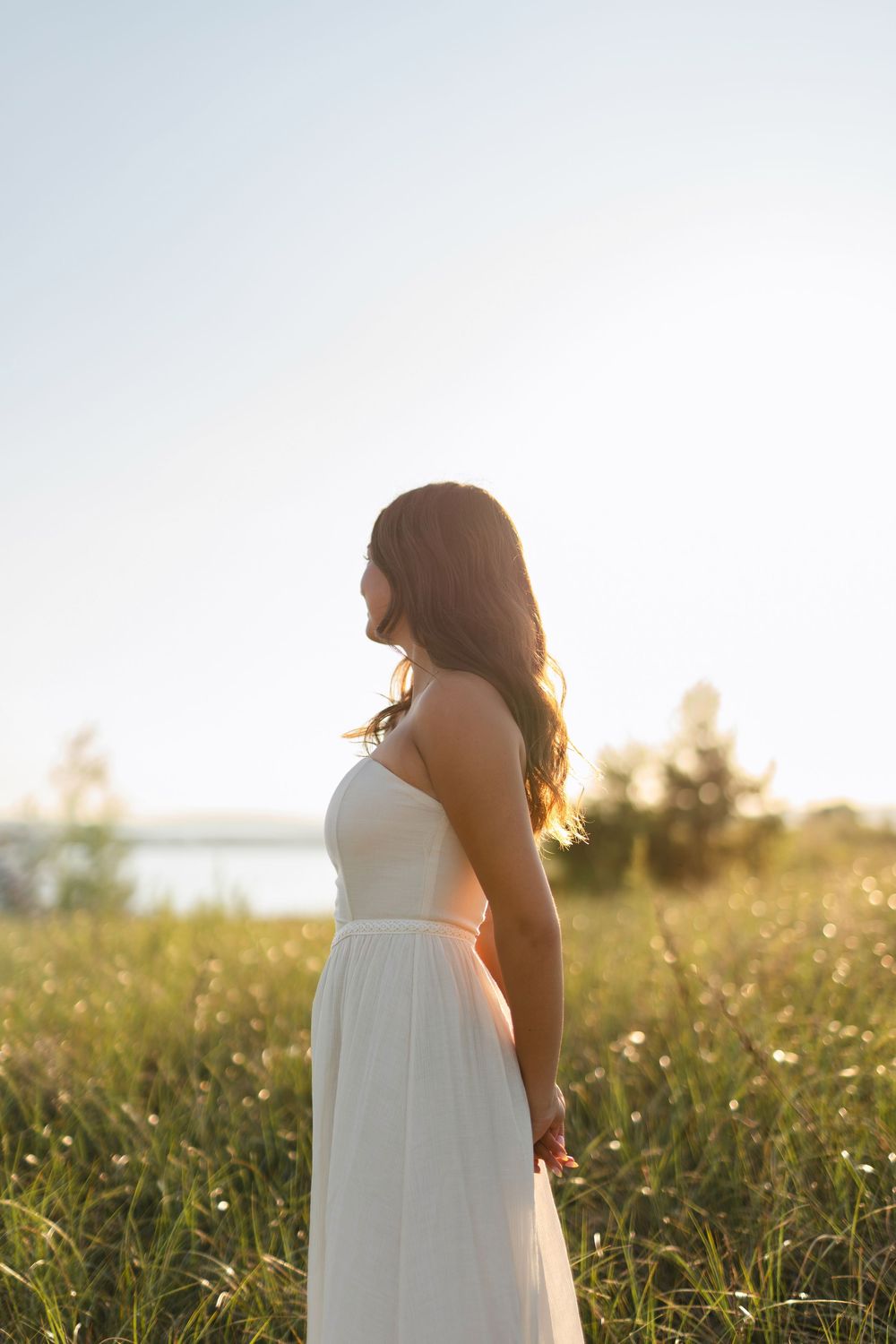 A white dress silhouette stands in a golden meadow at sunset with tall grass and wildflowers.