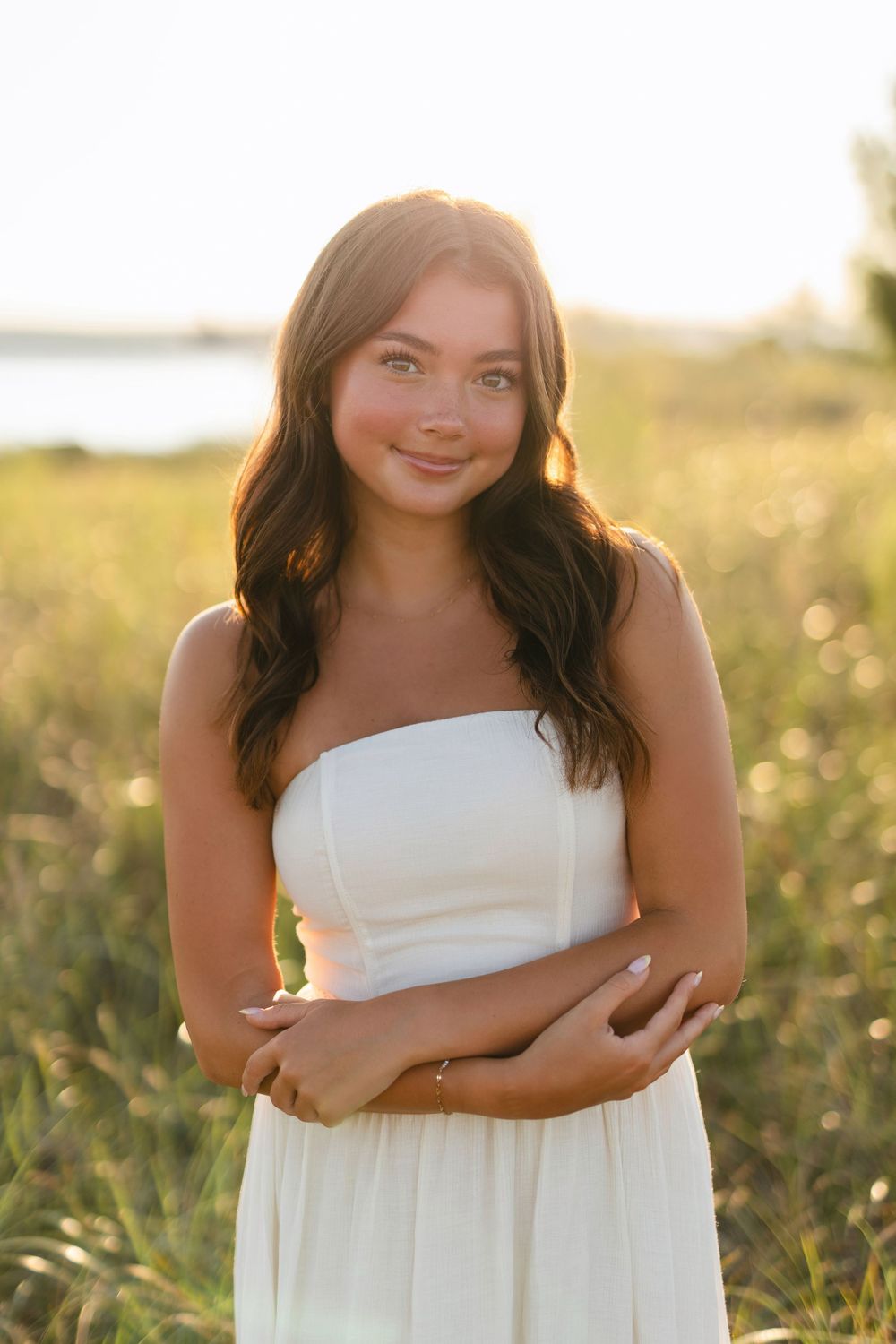 A woman in a white strapless dress poses in a golden field at sunset.