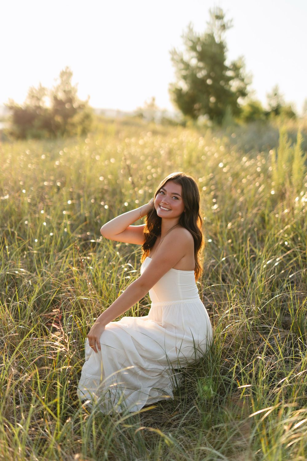 Person in white dress reclines in a summer meadow filled with wildflowers during golden hour.