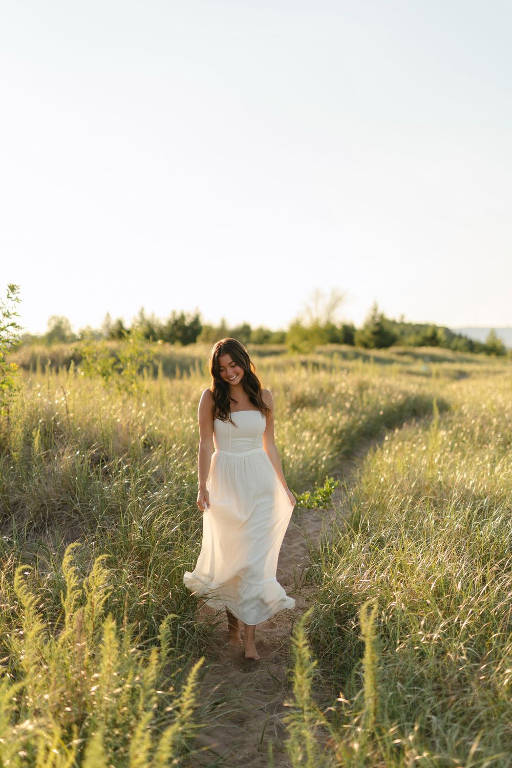 A flowing white dress catches the breeze among tall grasses in a sunlit field.
