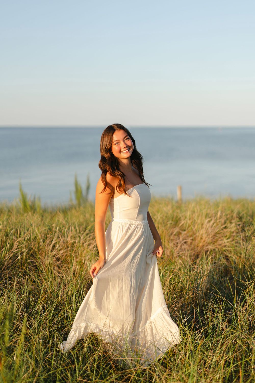A white summer dress flows in the breeze against an ocean backdrop during golden hour.