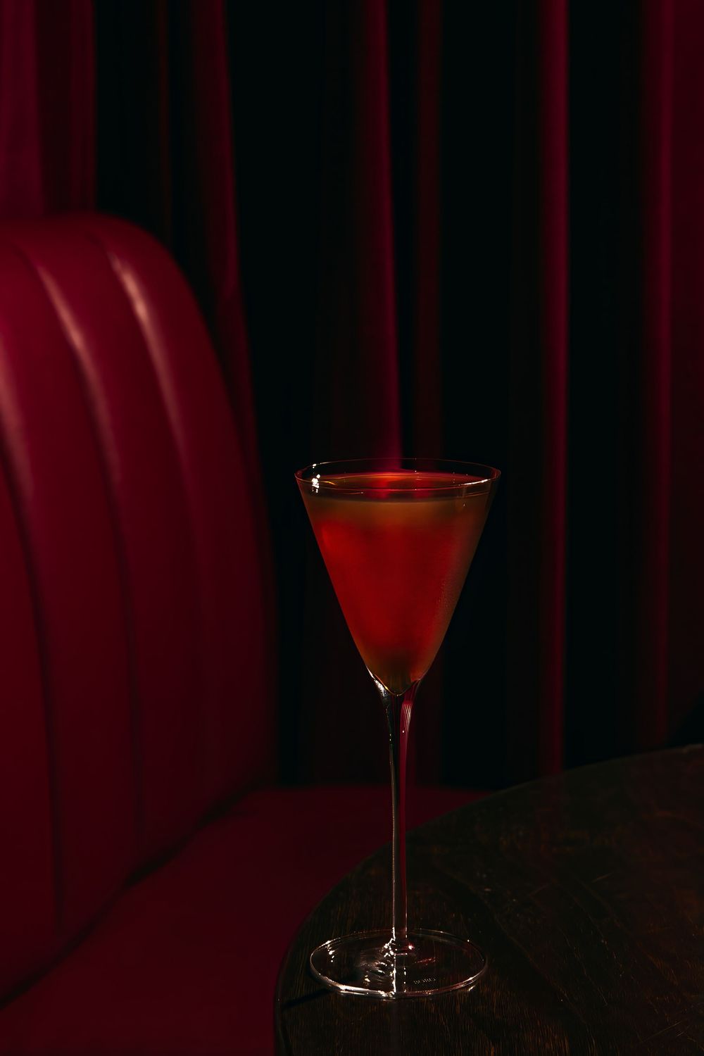 A cocktail glass filled with red liquid is photographed in a dramatic sequence against a dark red background.