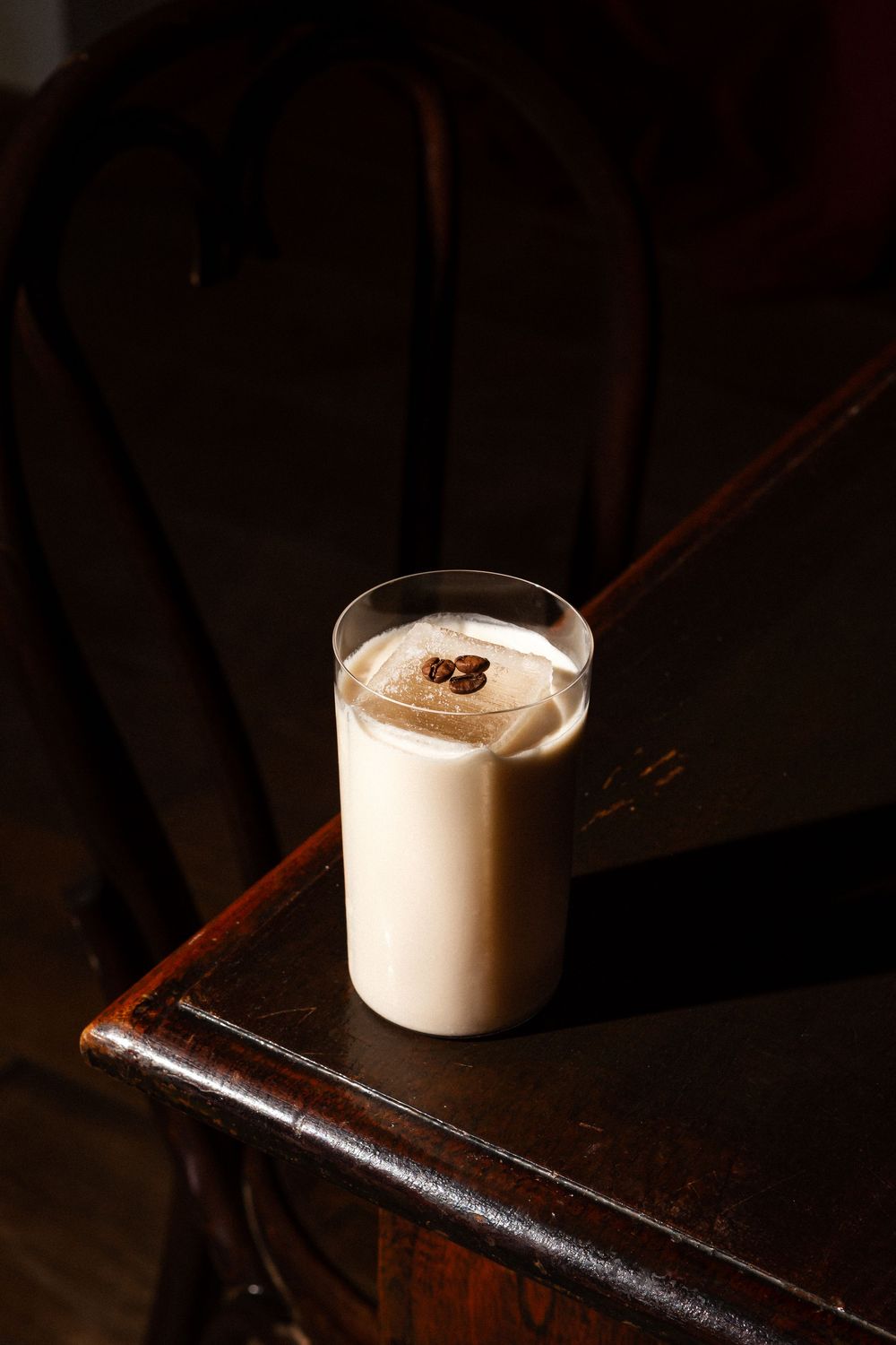 Coffee mousse with whipped cream and chocolate garnish served in a small glass on a dark wooden surface.