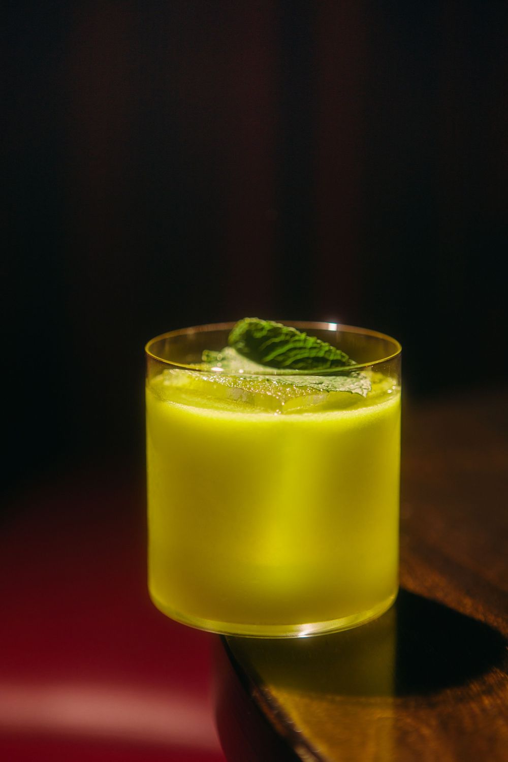 Four elegant yellow cocktails with mint garnish on a dark wooden surface in moody lighting.