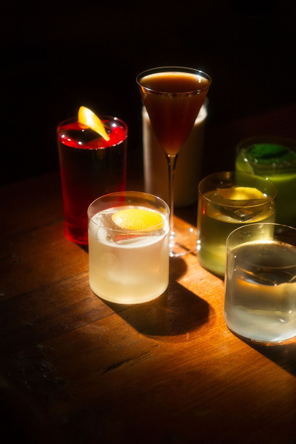 Illuminated cocktail glasses with glowing candles create a moody ambiance on a dark wooden surface.