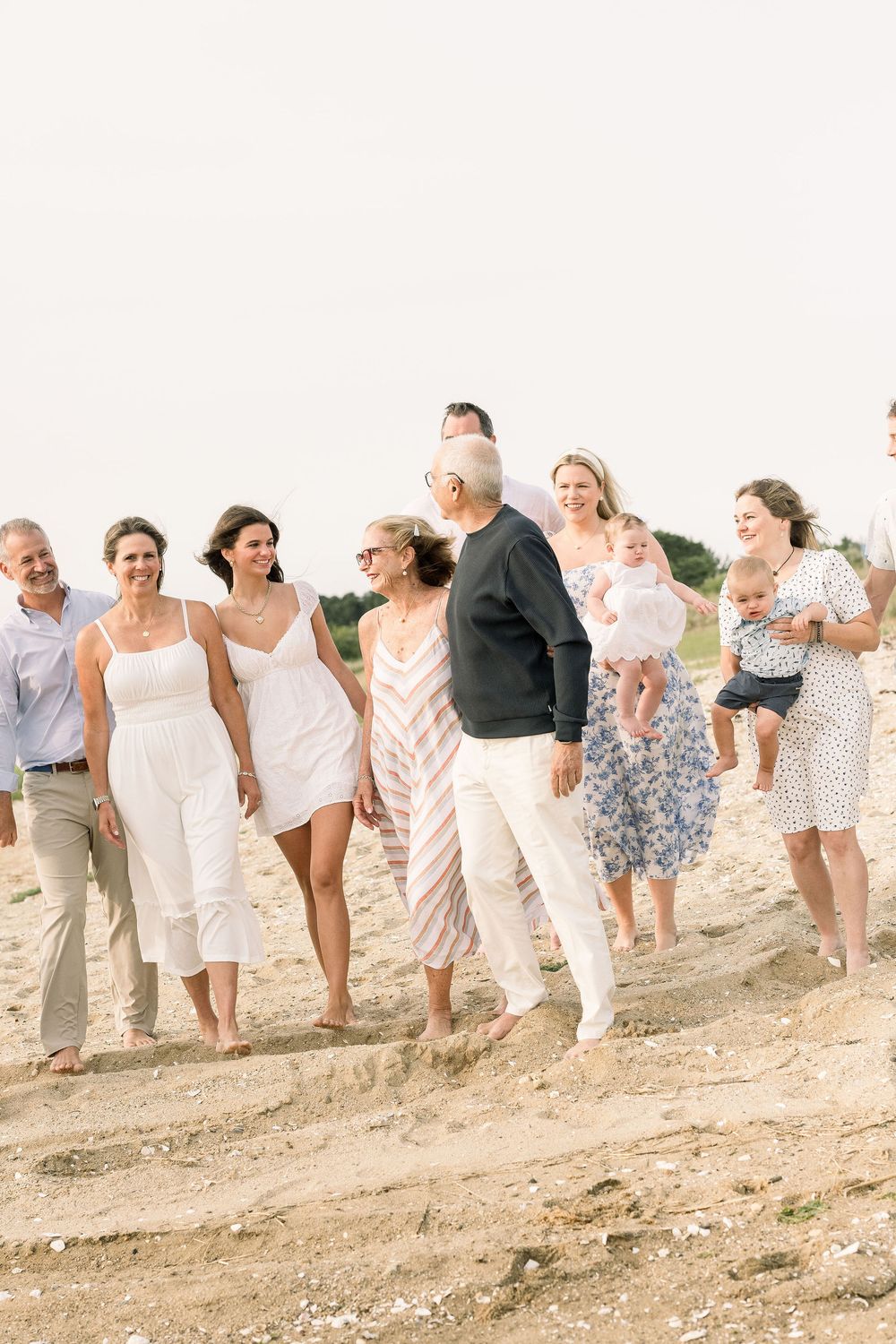 A group of people walking together along a sandy beach path wearing light summer attire.
