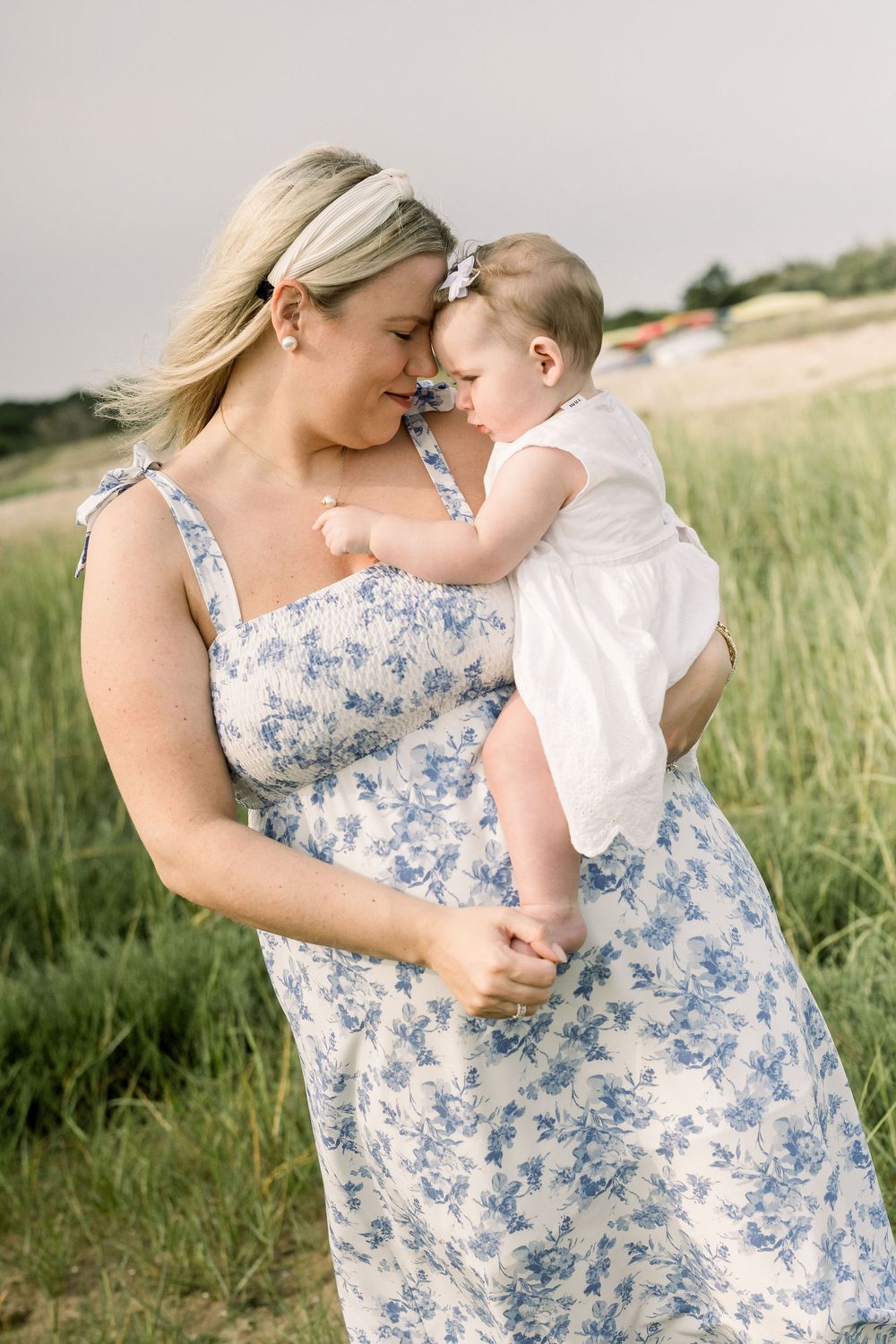 A tender moment between parent and child in a sunlit field with blue and white floral dress details.