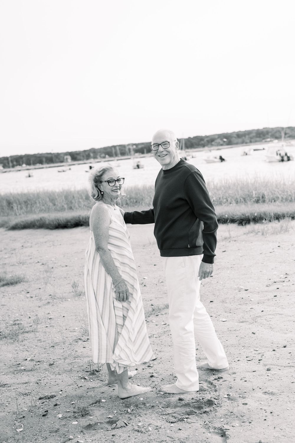Black and white sequence of a couple dancing playfully on a beach with grassy dunes in the background.