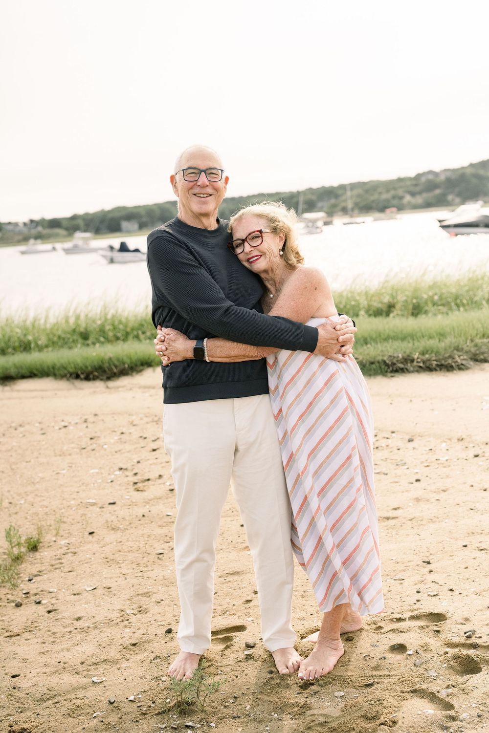 Romantic couple dancing and laughing together on a sandy beach with coastal vegetation in summer.