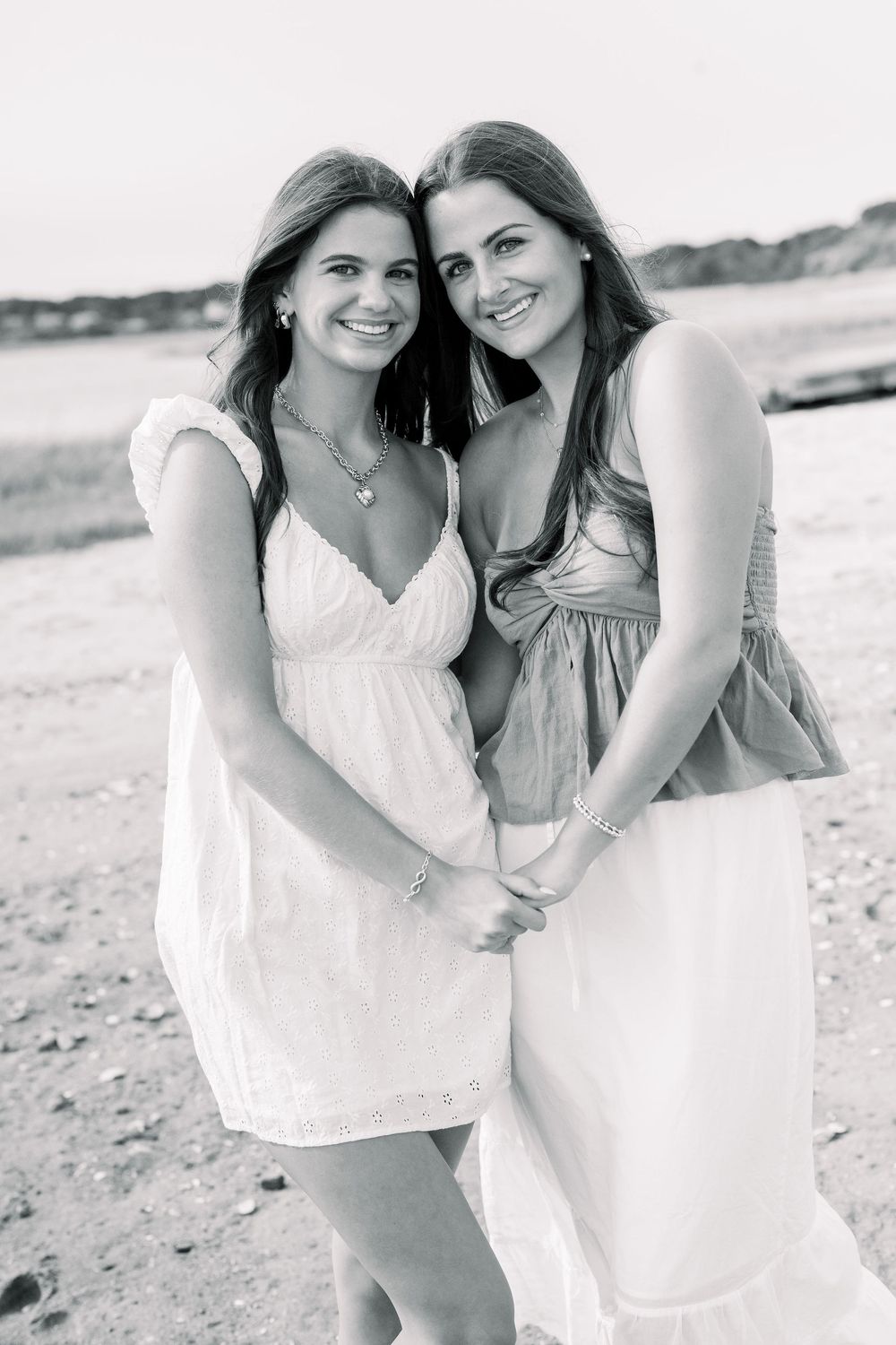 Black and white portrait of two friends in summer dresses smiling together on a beach.