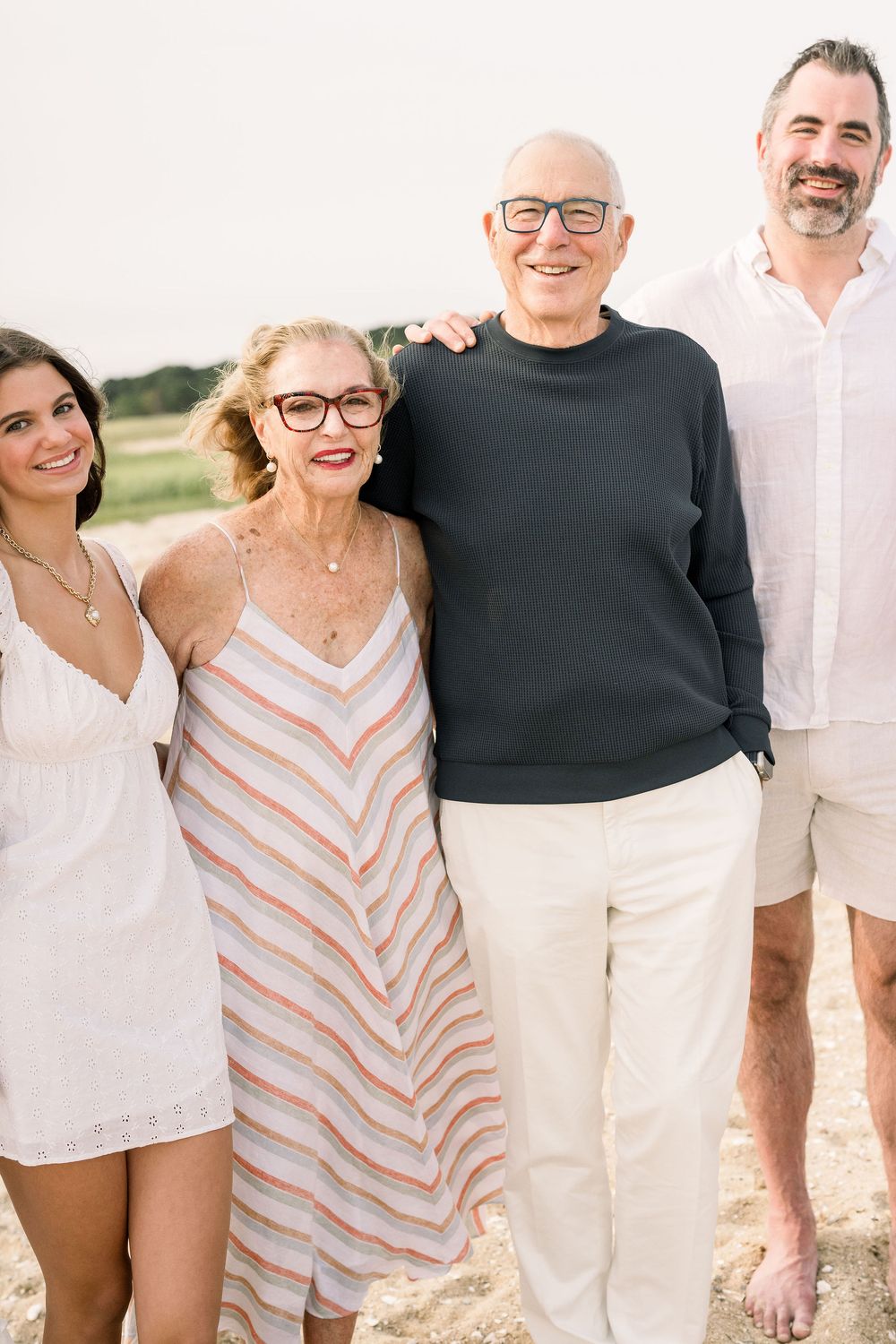 A group of people wearing casual summer attire pose together on a beach during golden hour.