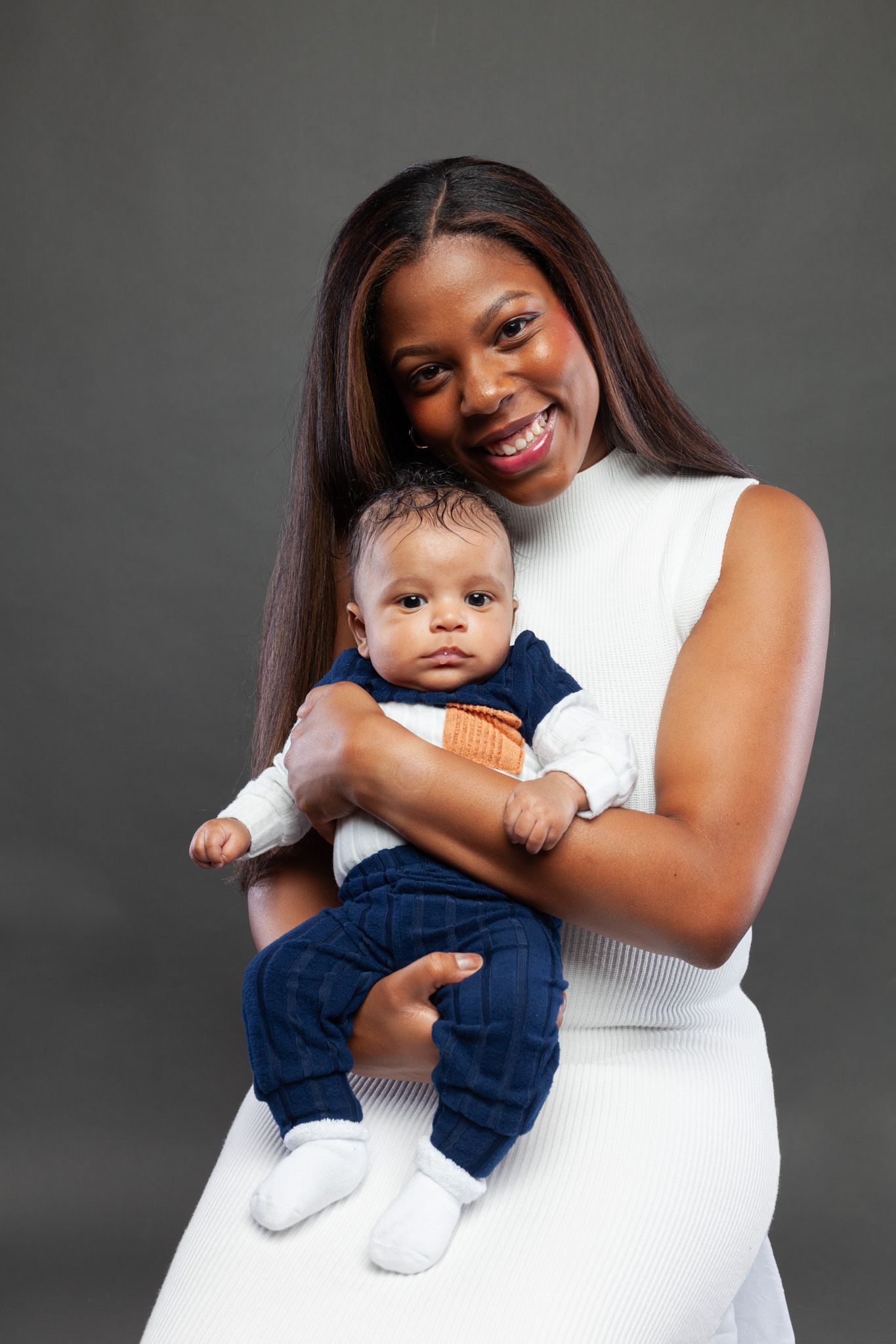 A mother in a white top embraces her baby wearing navy blue in a series of sweet studio portraits.