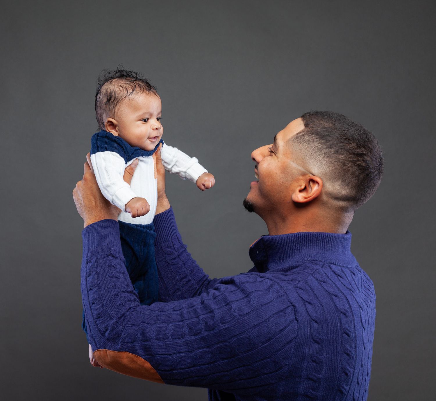 A sequence of photos shows a person in a navy sweater lifting and playing with a baby wearing white clothing.