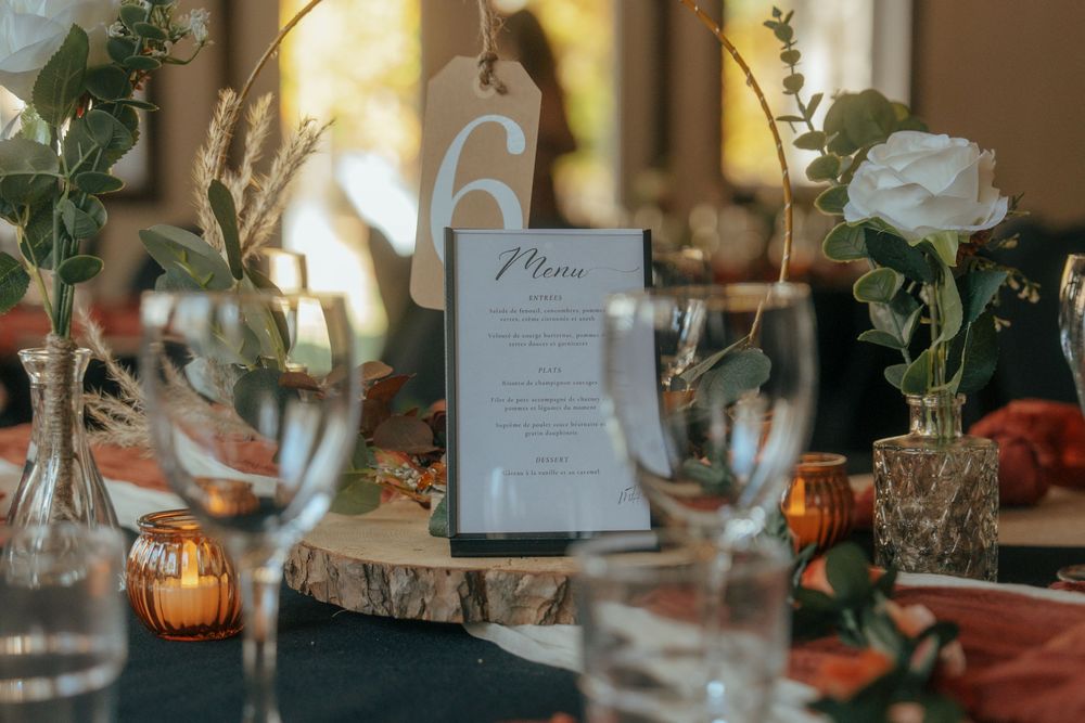 Wedding reception table decorated with greenery, white flowers, and amber glass votives in warm lighting.