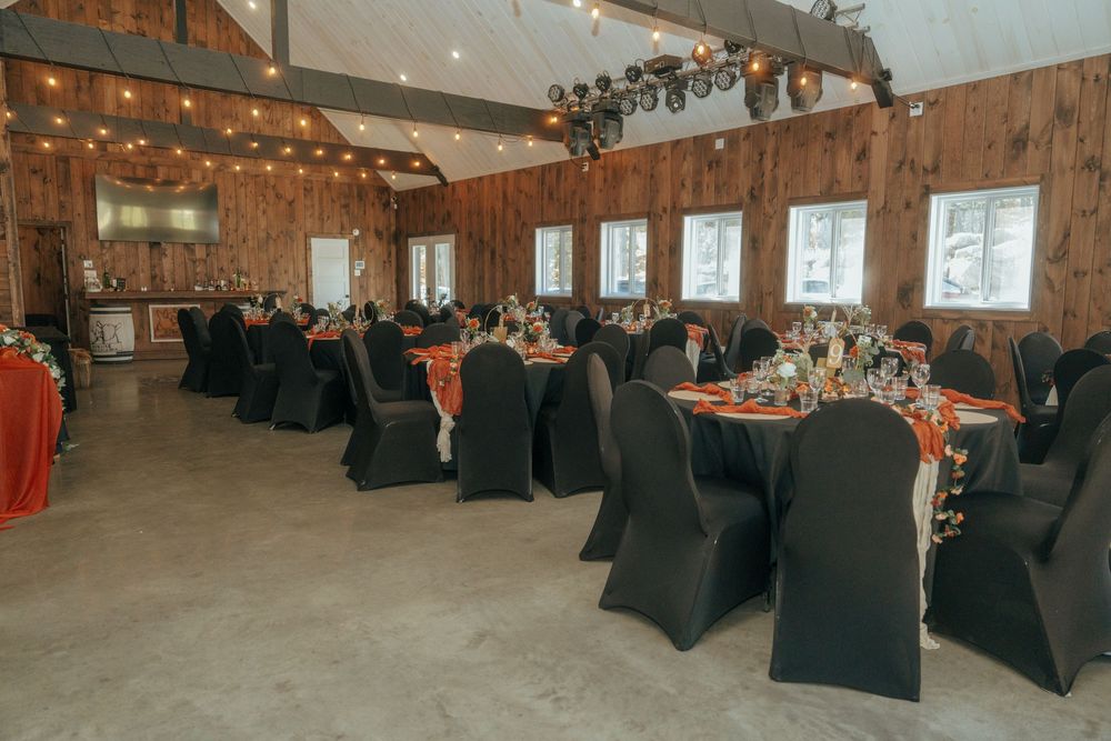 Reception venue decorated with black chair covers and string lights in a rustic wooden hall.