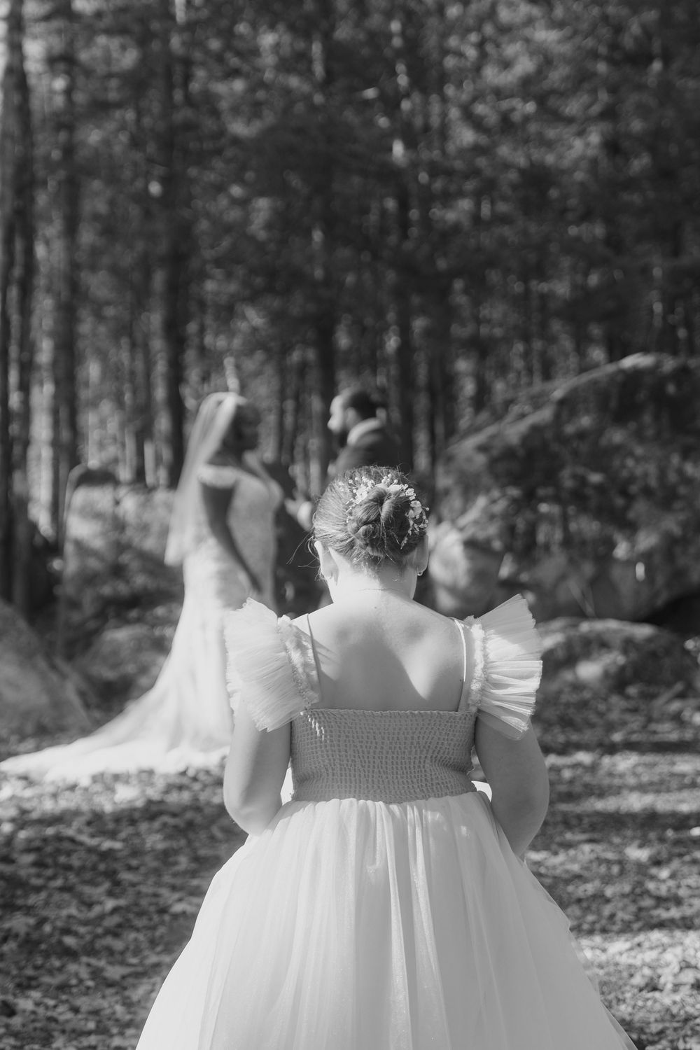 Back view of white ruffled dresses in a forest setting captured in black and white.