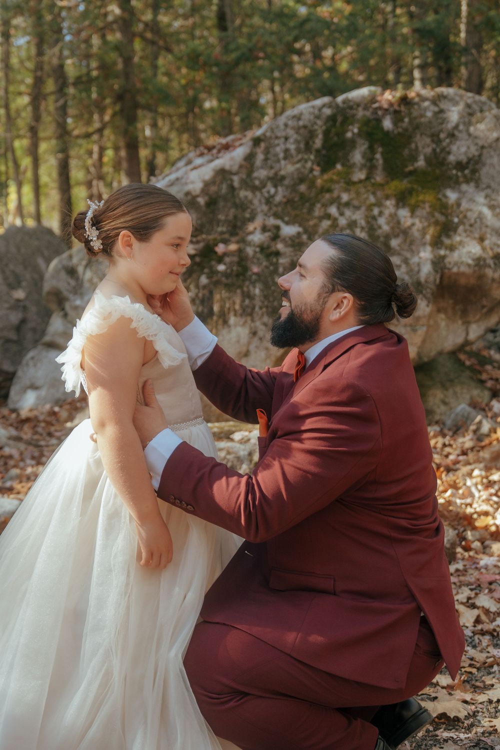 Wedding couple sharing an intimate moment among fallen leaves and large boulders in an autumn forest.