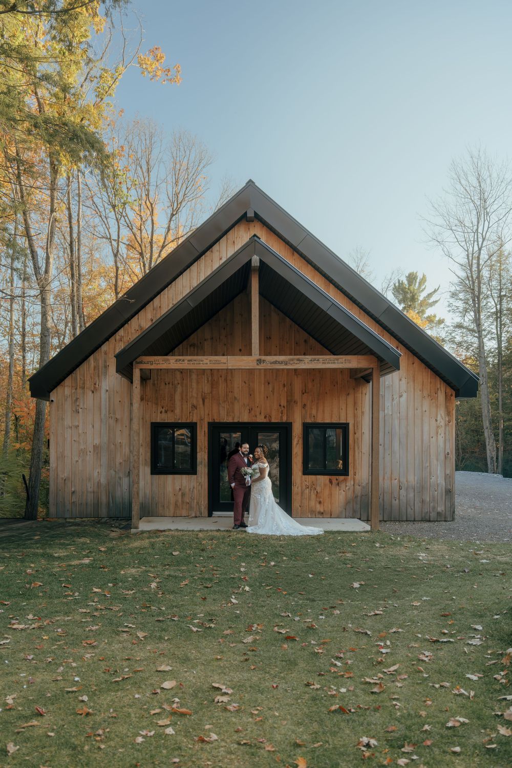 Modern wooden wedding venue with A-frame architecture surrounded by fall trees.