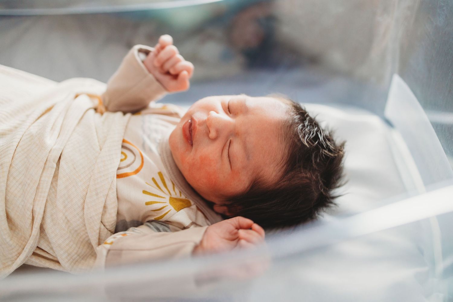 Peaceful sleeping baby in light colored onesie lying on white bedding.