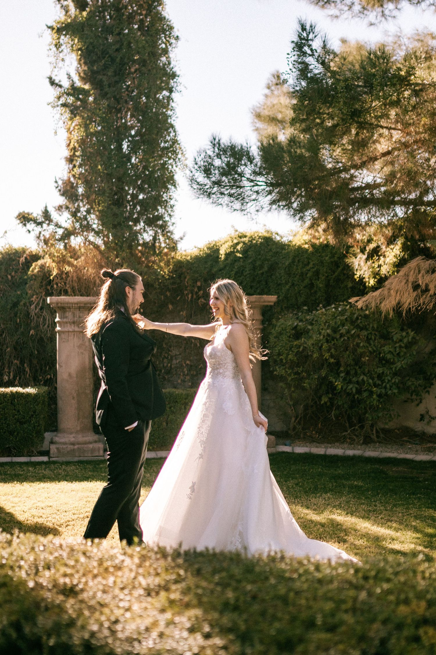 A couple in wedding attire walks together on a sunlit lawn during golden hour at their outdoor ceremony.