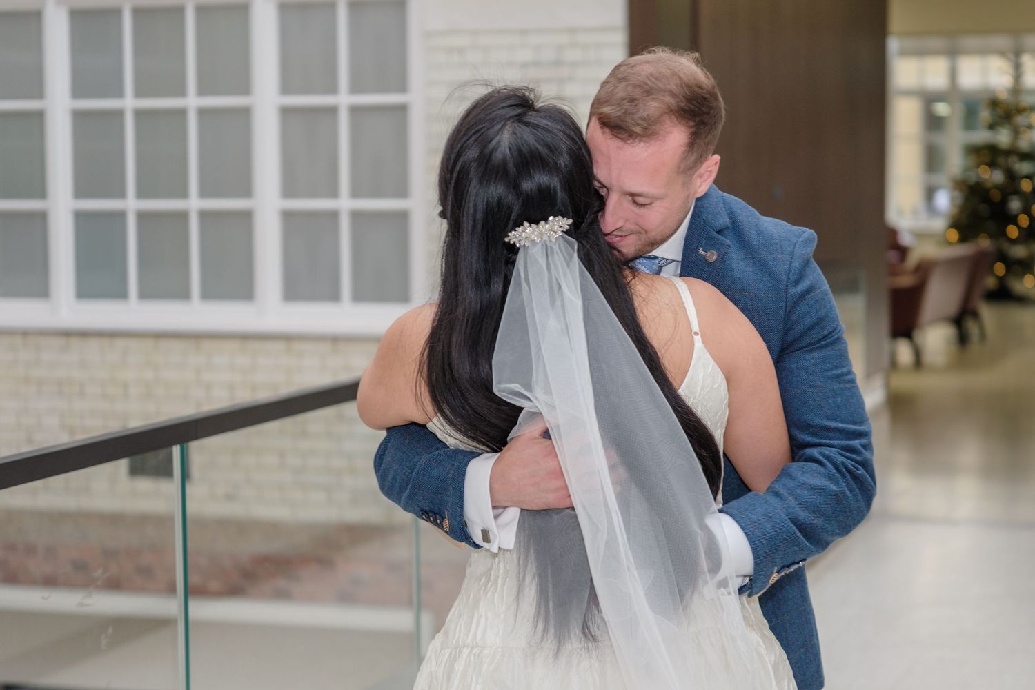 A tender first look moment between newlyweds as the groom embraces his bride wearing a flowing veil and white dress.