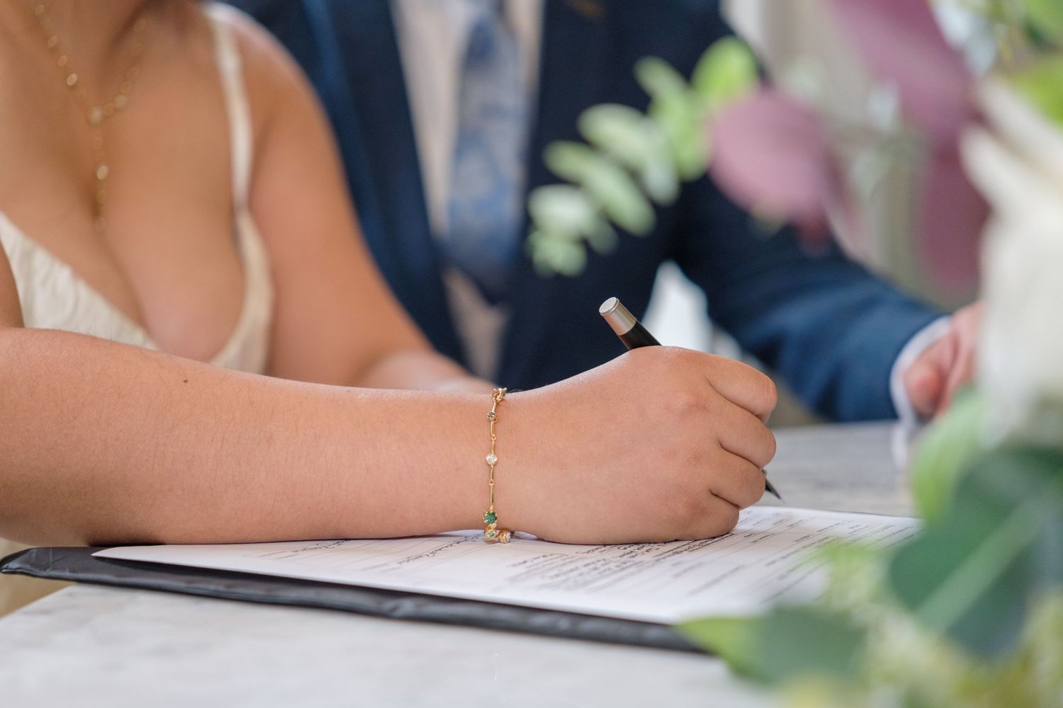 A person signs a document at a wedding ceremony table decorated with delicate floral arrangements.