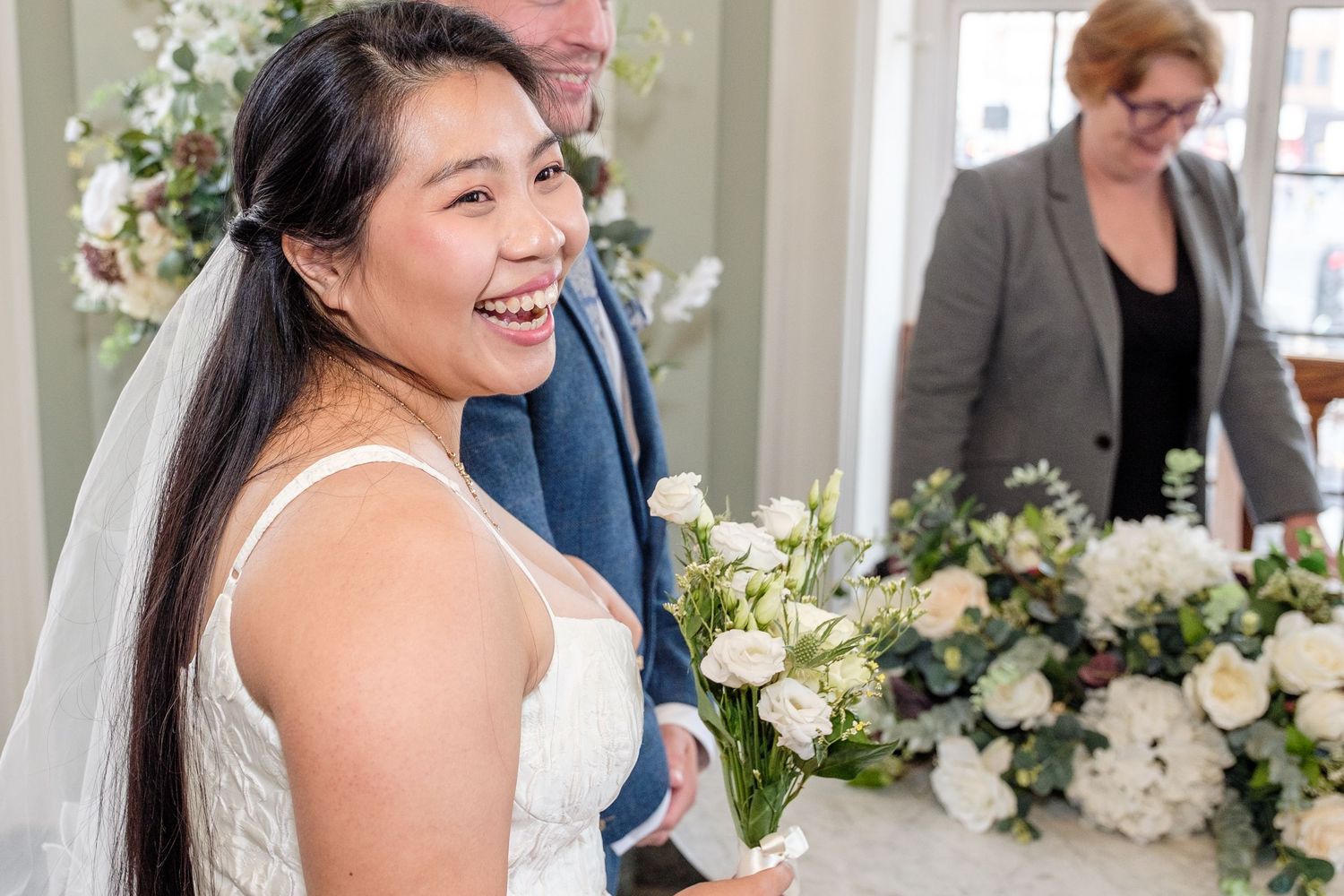 Joyful wedding celebration with elegant white floral arrangements and natural light streaming through windows.