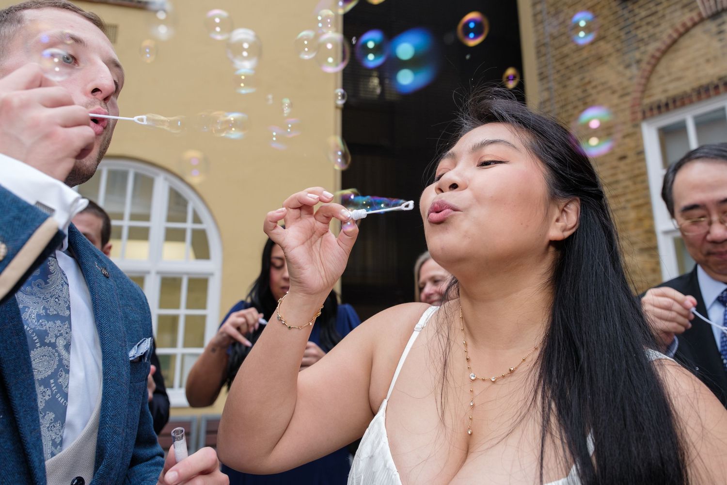 Wedding guests blow bubbles during an outdoor celebration creating a magical atmosphere at a historic venue.