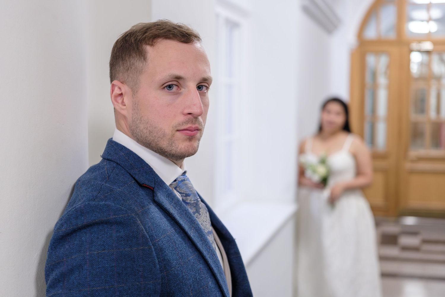 Wedding party members in navy suits and white dresses gather for formal portraits in bright indoor setting.