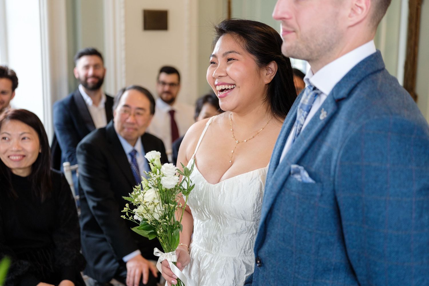 Joyful wedding celebration with guests smiling and laughing during an indoor ceremony.