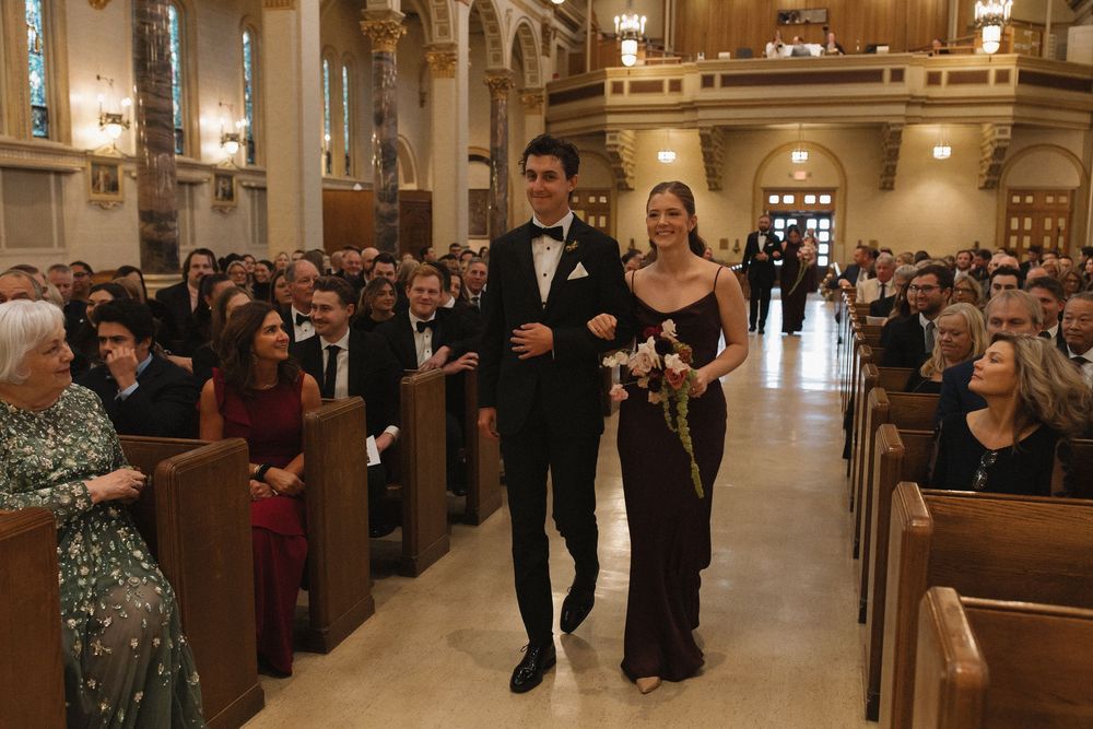 Wedding guests walk down the aisle of an ornate church during a formal ceremony.