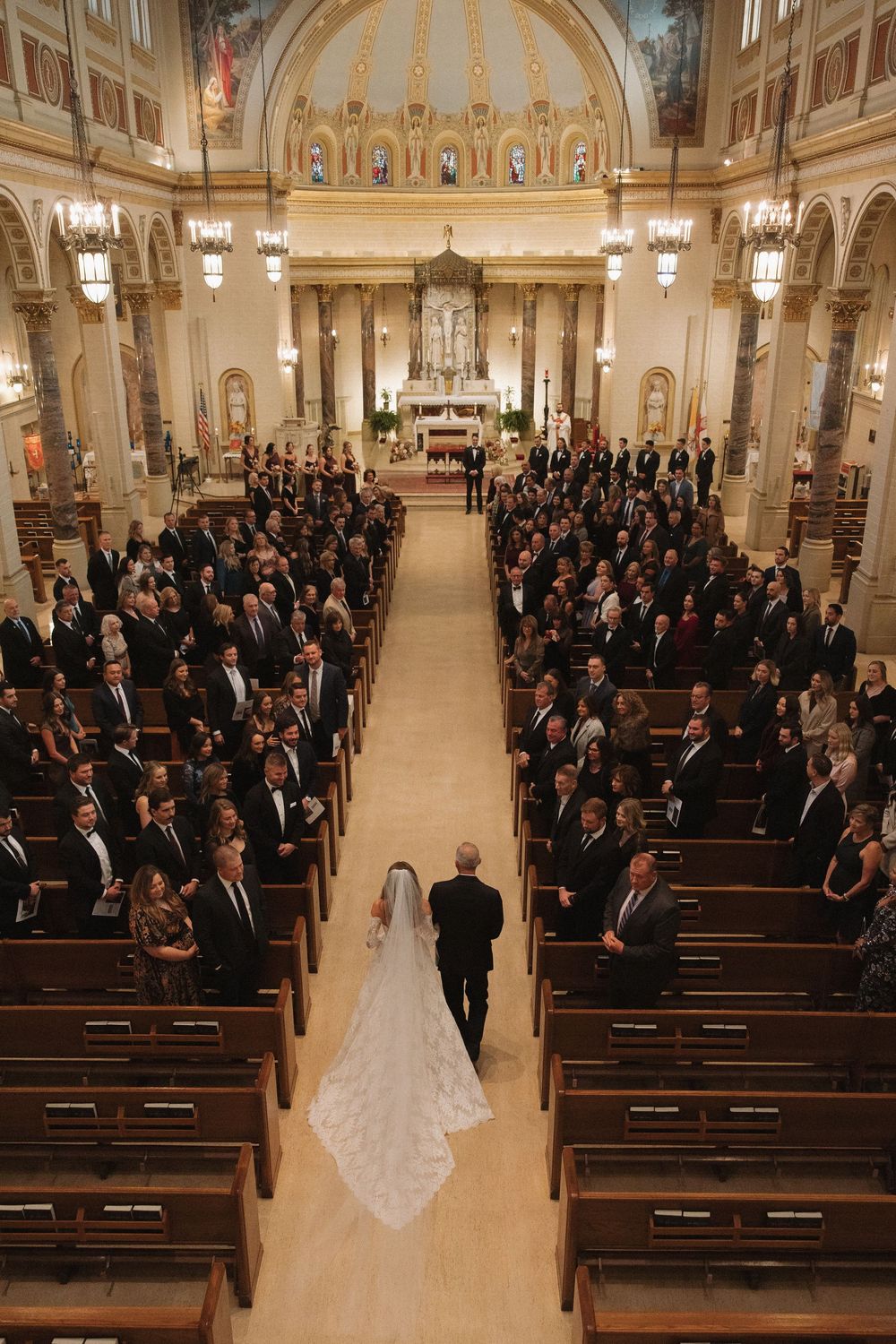 A grand church filled with wedding guests seated in wooden pews beneath a decorated dome ceiling.
