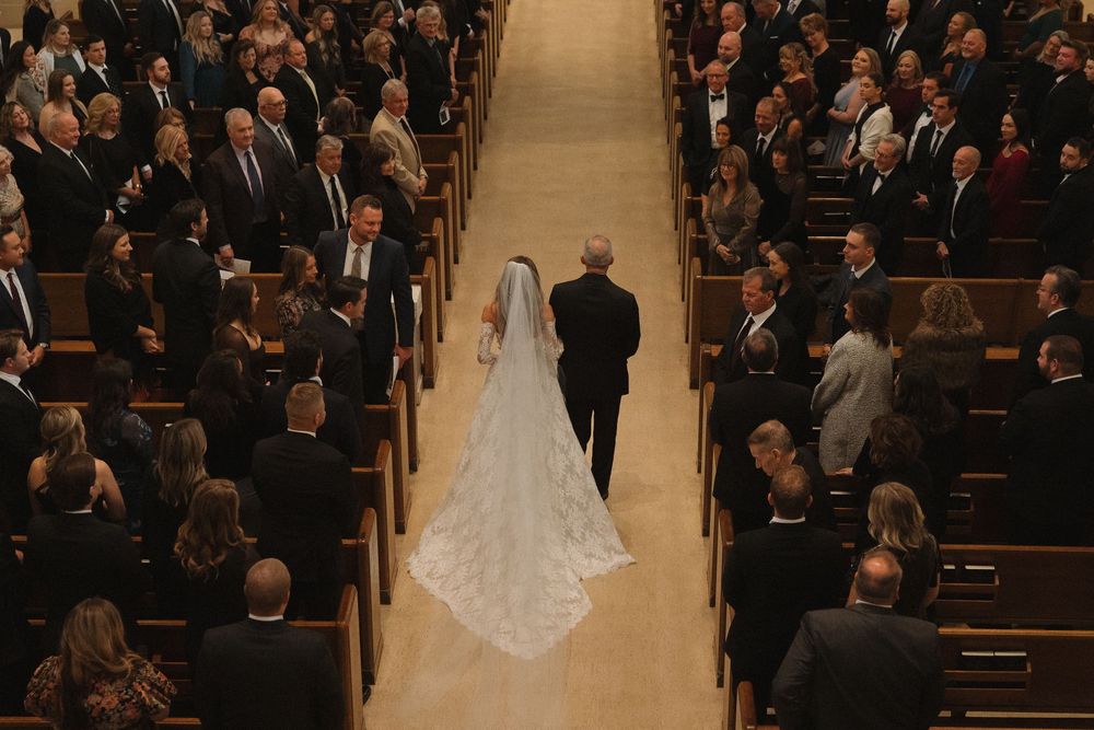 A wedding ceremony in a traditional church with guests seated in wooden pews and a bride walking down the aisle.