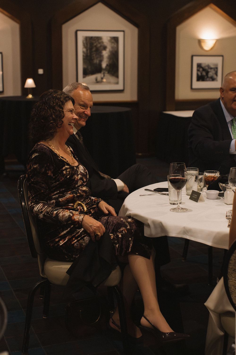 People enjoying a formal dinner at an elegant restaurant with white tablecloths and framed artwork on the walls.