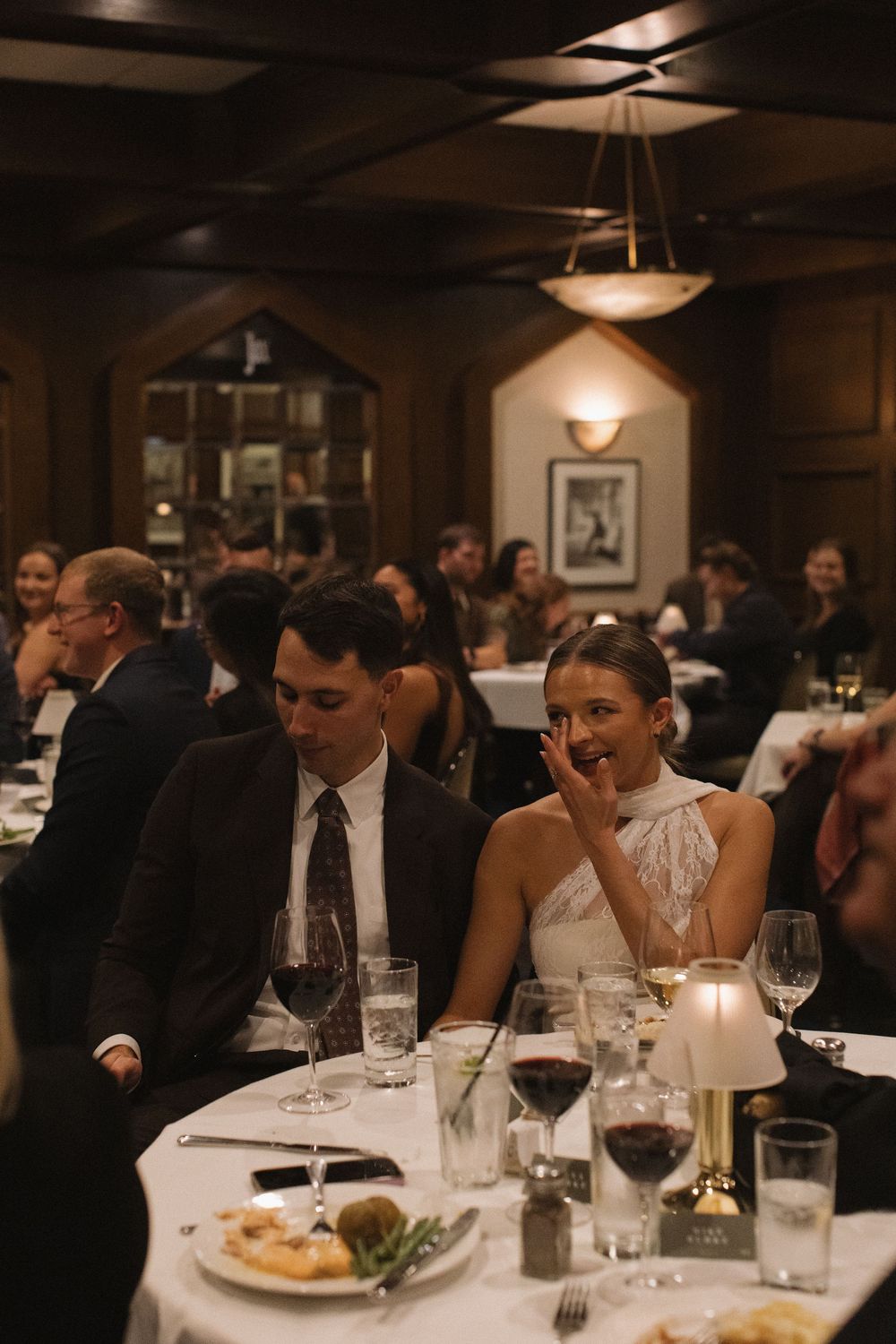 Elegant dinner party at an upscale restaurant with guests seated at tables with white tablecloths and wine glasses.