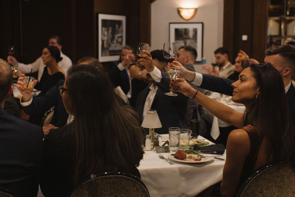 A group of people raise their glasses in a toast during a formal dinner event at a dimly lit restaurant.