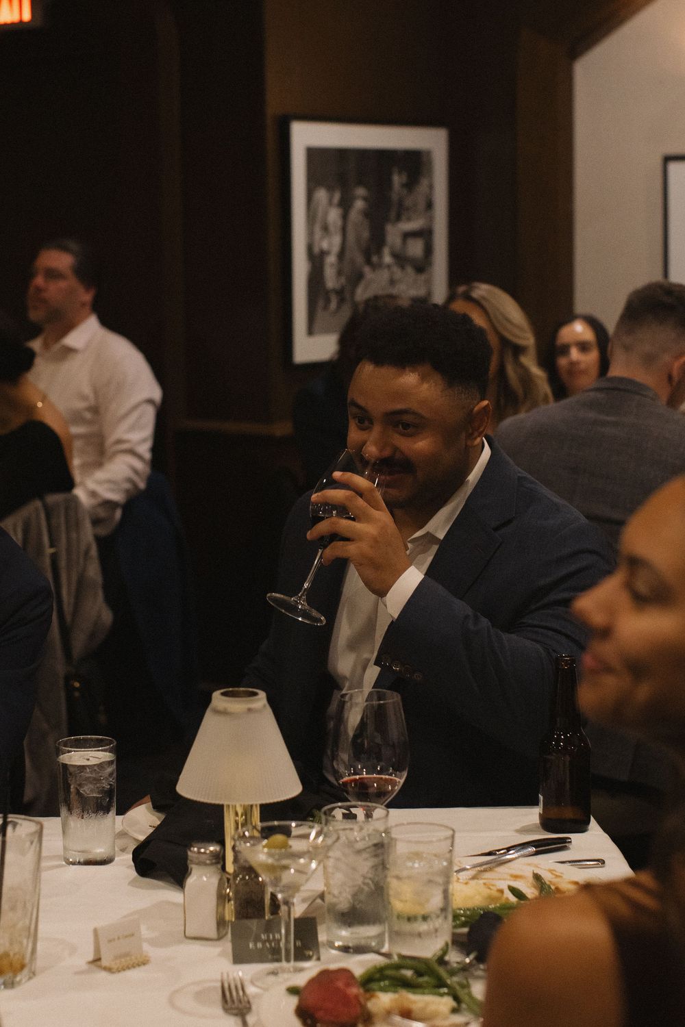 People gathered around a dining table with glasses and plates at an evening event.