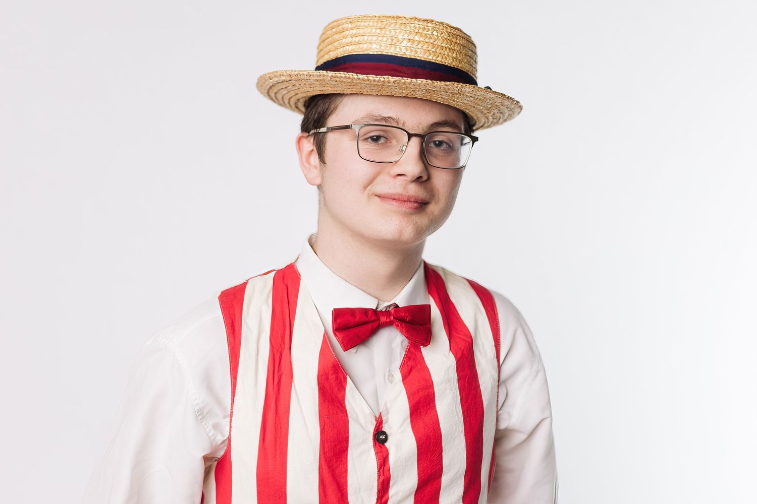 Four performers in matching red and white striped vests and straw boater hats pose against a white background.