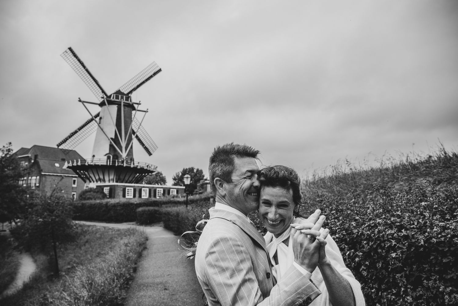 Zwart-wit portret van trouwkoppel bij historische molen in Willemstad, Nederland, vastgelegd door Bart Boodts met focus op emotie.