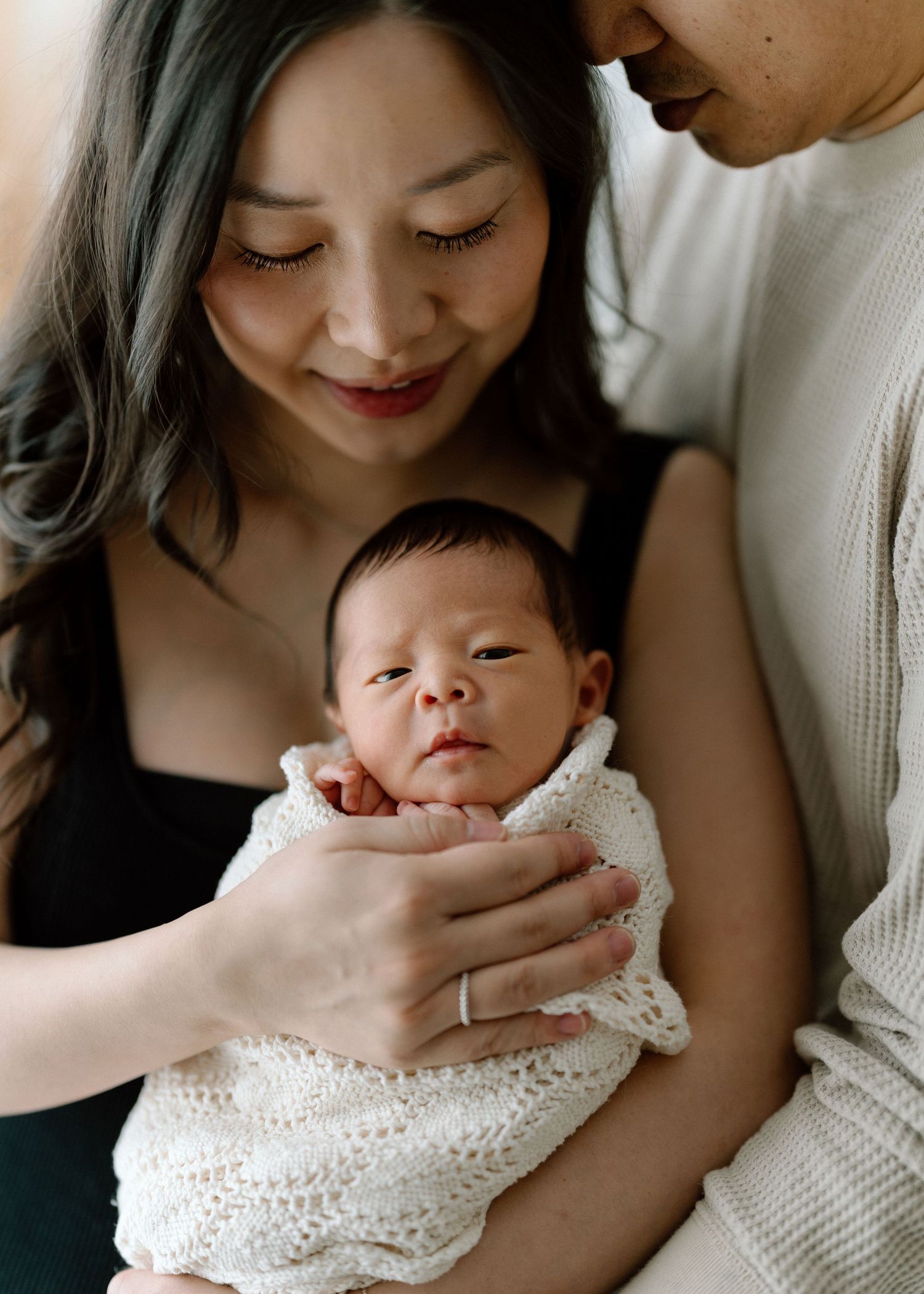 Newborn baby wrapped snugly in soft white swaddle blanket against light background.