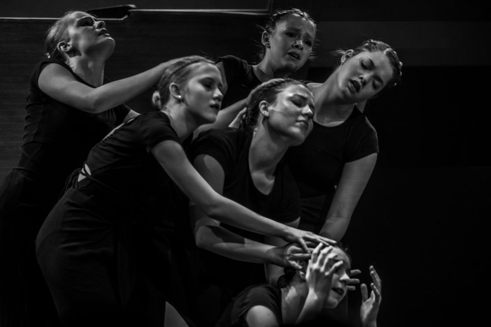 Dancers in black costumes create dynamic shapes through modern dance movements on a dark stage.